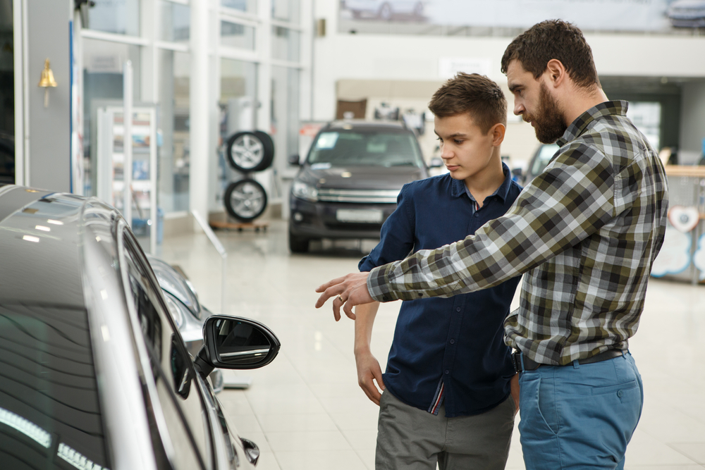 A person holding a car key while standing outside a car dealership