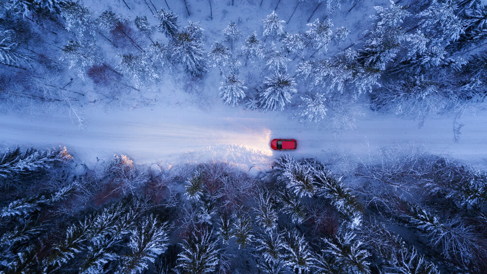 A red car driving down a winter roads, with its headlights shining bright